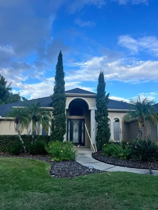 The front entry of a stucco house with columnar junipers either side, a trimmed hedge, fresh dark mulch beds and a clear walkway.